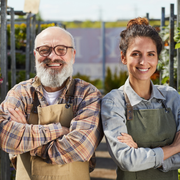 Happy man and woman workers standing in plant nursery garden.